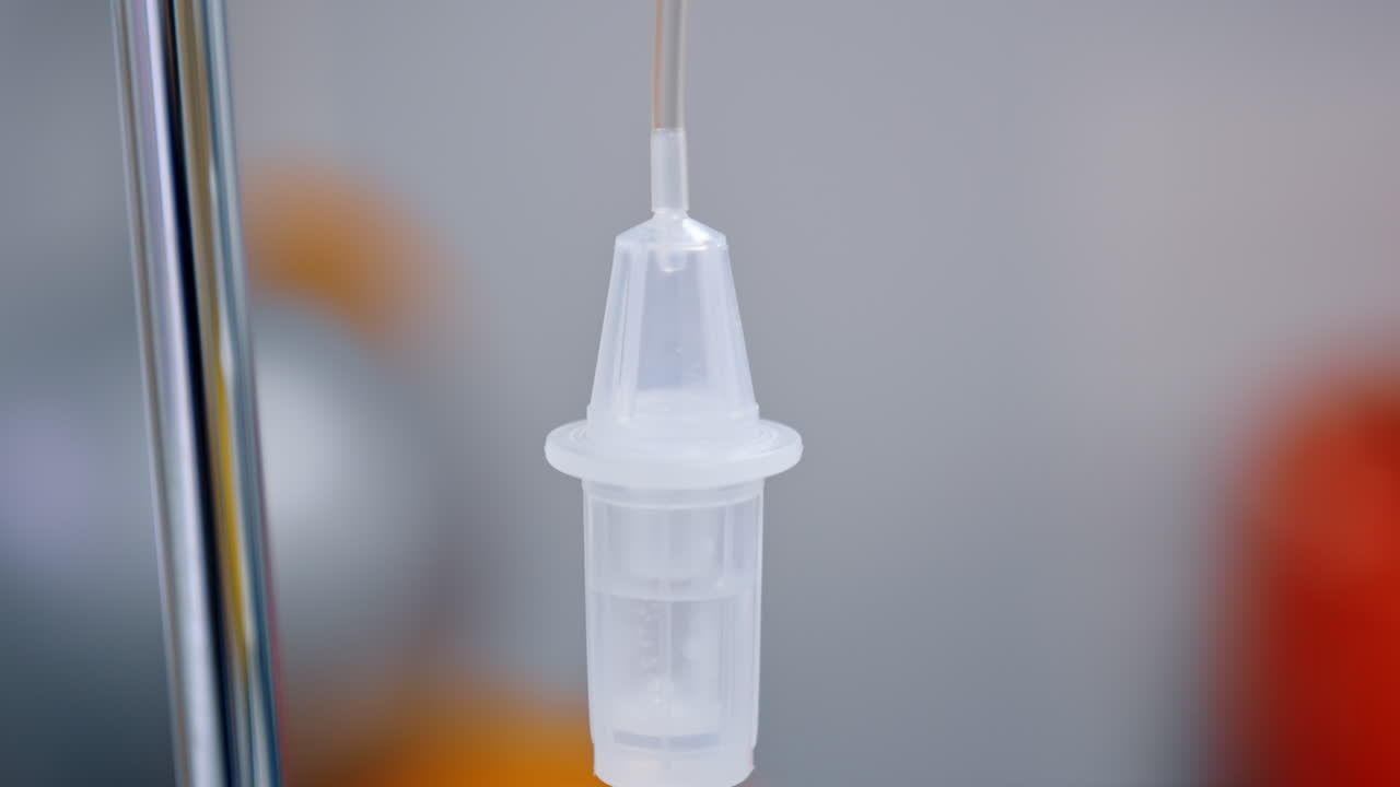 Liquid medicines slowly dripping inside the reservoir of drop counter. Medical equipment close up.