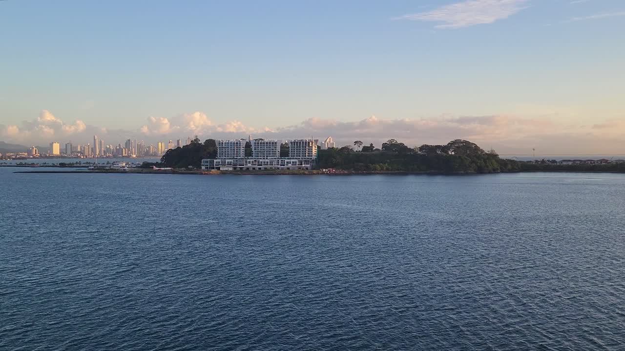 A beautiful scenic view across the tranquil ocean shows Naos Harbour Island on the Amador Causeway, with the modern Panama City skyline visible in the distance under a golden sky.