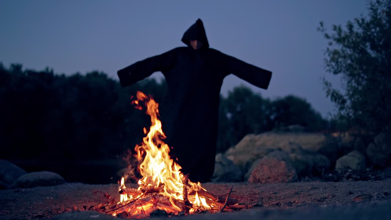 The wicked witch performs a ritual near a bonfire in the night. Mysticism of Halloween