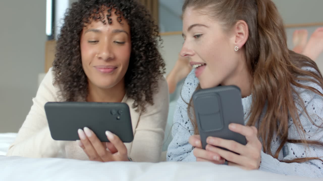 Using smartphones, lesbian couple relaxing on bed and enjoying time together