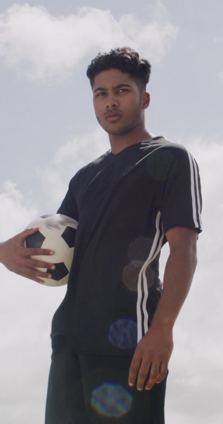 Joven futbolista sosteniendo un balón al aire libre