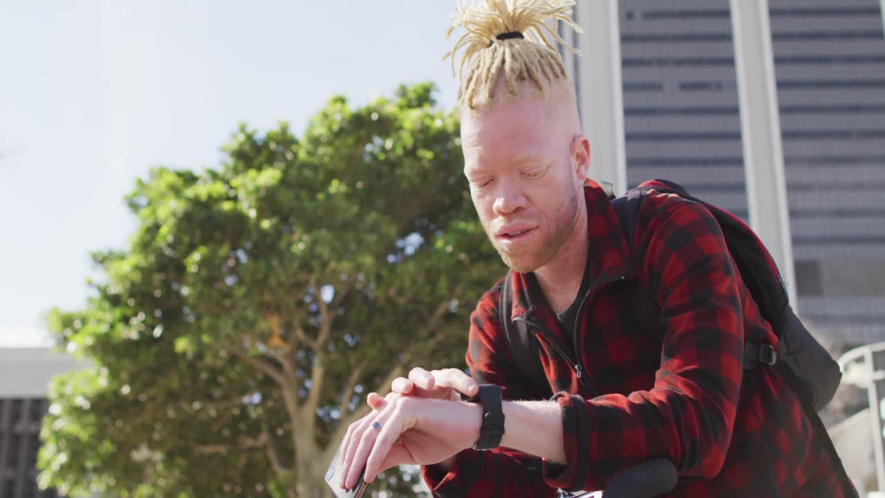 hombre albino afroamericano pensativo con rastas usando reloj inteligente y teléfono inteligente