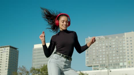 empowered happy young attractive latin woman enjoy dancing listening to trap dance music with wireless red headphones on a sunny day at the city