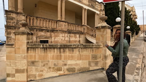 Shot-of-woman-waiting-at-sign-infront-of-architecture-building