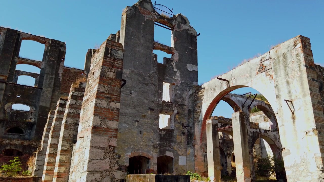 Ruínas históricas da Hacienda Coahuixtla, apresentando paredes de pedra desgastadas, arcos altos e os restos de uma antiga propriedade colonial sob um céu azul claro em Morelos, México.