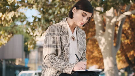 female entrepreneur drawing up business plan for a month in notepad while resting outdoor.