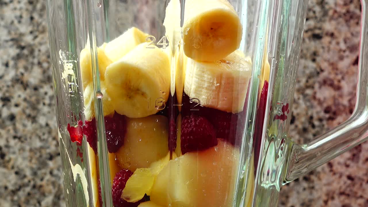 Fyller blenderen med biter av pære, bringebær og bananer