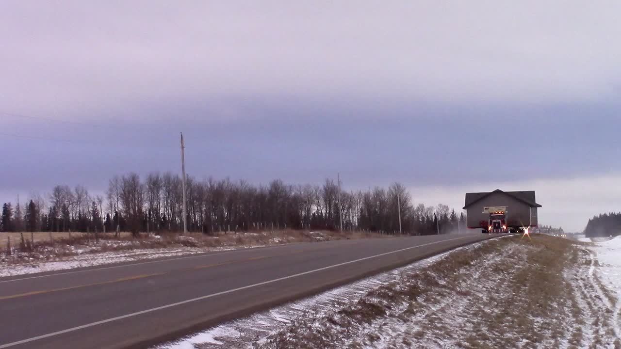 Slomo of a house being moved by truck down a highway in the winter
