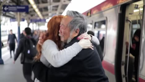 a woman joyfully embraces an elderly man at a train station while people rush by. their heartfelt reunion captures a moment of love and connection during a busy afternoon.