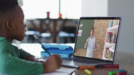 niño afroamericano haciendo la tarea mientras tiene una videollamada con un profesor masculino en una computadora portátil en casa