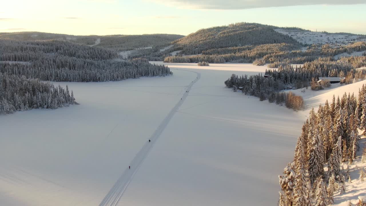 Veduta aerea ad alta quota di sciatori su un lago ghiacciato e montagne sullo sfondo.