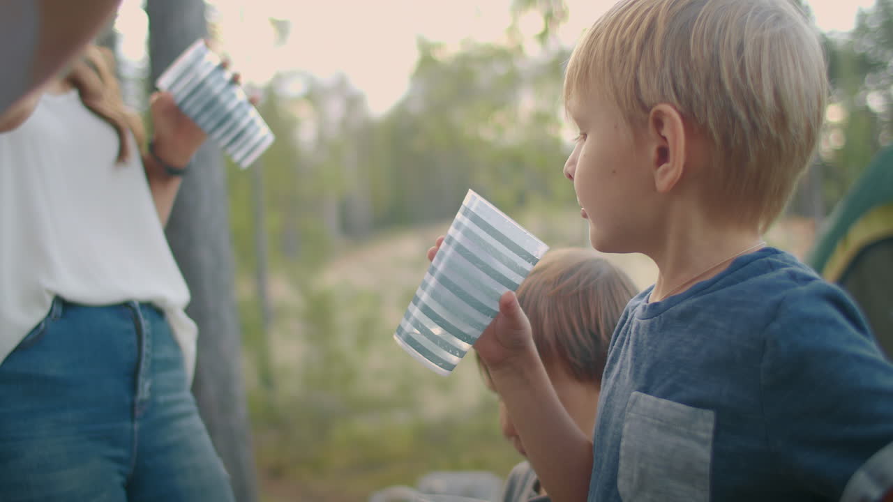 la familia está descansando en el campamento de la naturaleza en el bosque con una tienda de campaña los niños pequeños están bebiendo agua vacaciones de verano