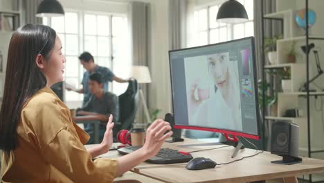asian female digital editor stretching while works in photo editing software on her personal computer with big display in office