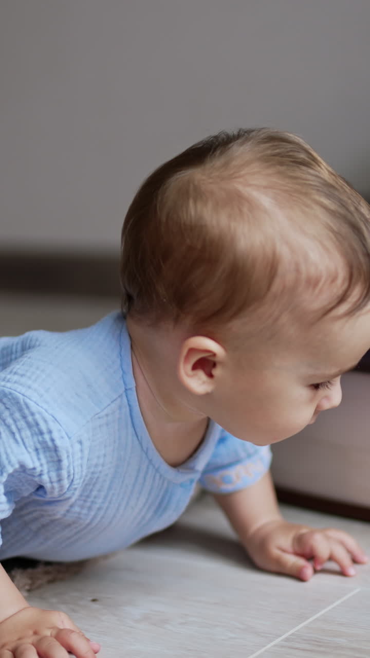 Sweet adorable baby boy crawling by the floor indoors. Active healthy kid trying to reach a ball. Little kid playing with a toy. Vertical video