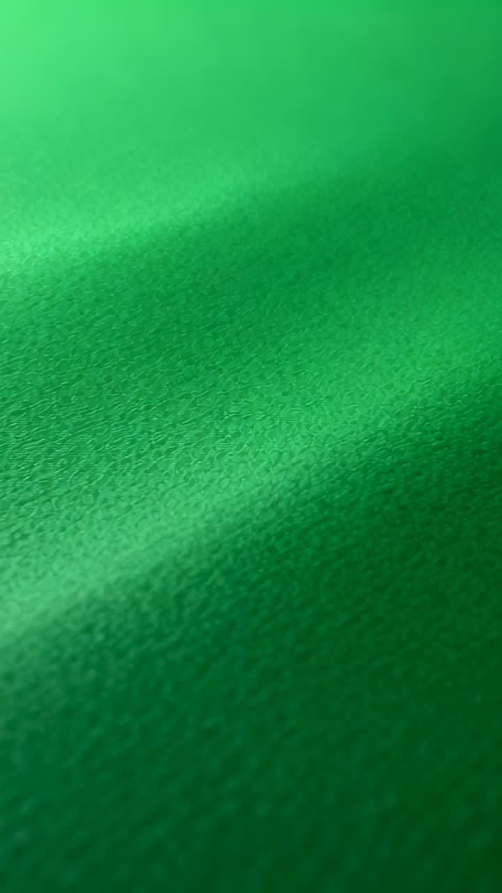 Vídeo vertical: Câmera se inclinando, resultando em uma varredura em close-up, mostrando a mudança de foco em um tecido verde texturizado.