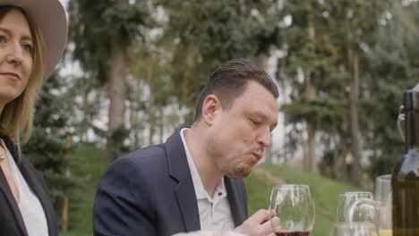 middle aged man and woman eating and talking to his friends sitting at table during an outdoor party in the park