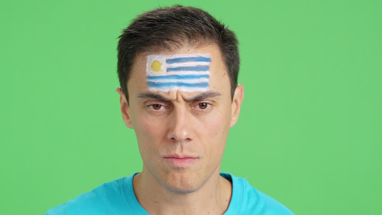 Serious man with a uruguayan flag painted on the face