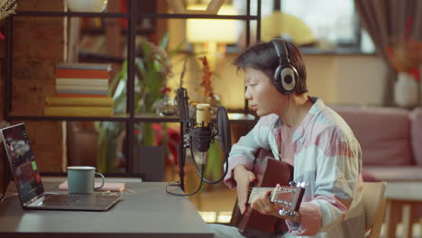 asian woman playing guitar and recording song in home studio