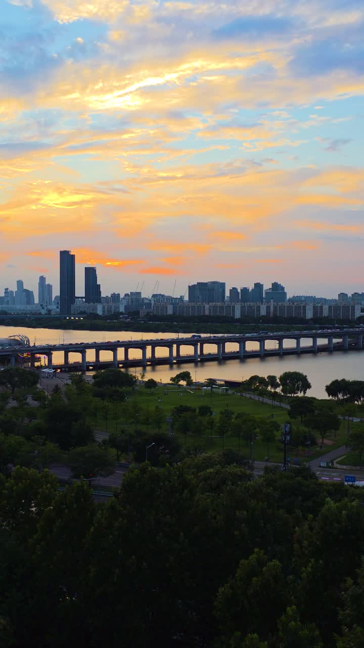 Vertical aerial drone shot zooms in on Seoul's Banpo Bridge and Han River, capturing the beautiful cityscape under a golden sunset sky