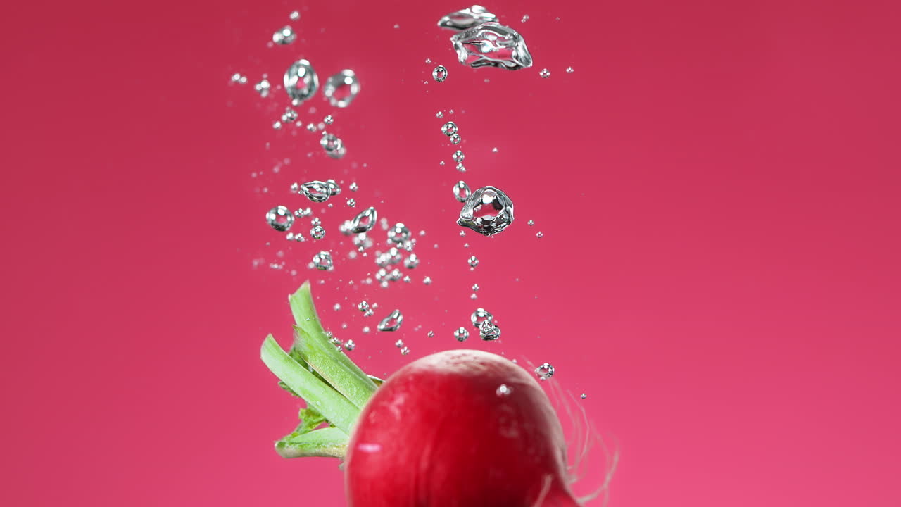 rábano caído en el agua hace burbujas y se hunde al fondo en fondo rosa, cámara lenta y macro