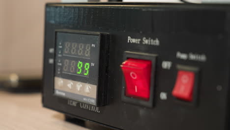 a close-up view of a technician's gloved hand pressing the red power switch off on a black temperature control device