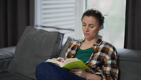 young pretty woman reading book while sitting on sofa at home