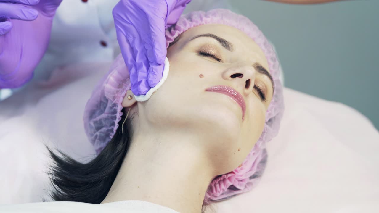 Medico estetico che deterge la pelle della donna con una spugna. Pulizia perfetta - trattamento viso spa per la cura della pelle