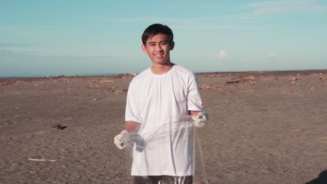 Child-Looking-At-Camera-With-Gloves-And-Holding-Plastic-On-The-Beach