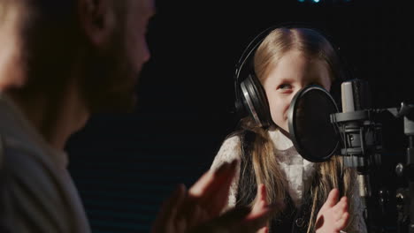 hombre aplaude a la niña en el estudio de audio. niña feliz terminando la lección de voz con un mentor profesional. fin del duro día de entrenamiento en la escuela de música