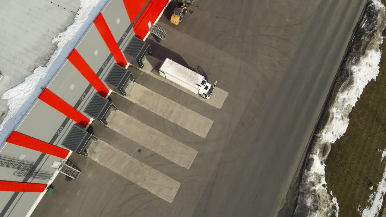 Aerial view of a logistics truck preparing to reverse into a warehouse loading dock at a modern distribution center during daytime operations