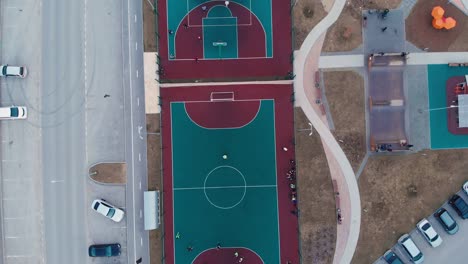 the drone descends on a sports ground in the yard, people play on the sports ground in their free time, next to a skateboard court with young people