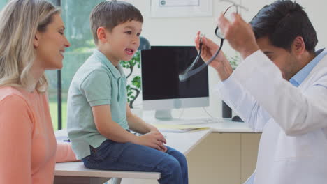 doctor or gp in white coat meeting mother and son for appointment in office listening to chest