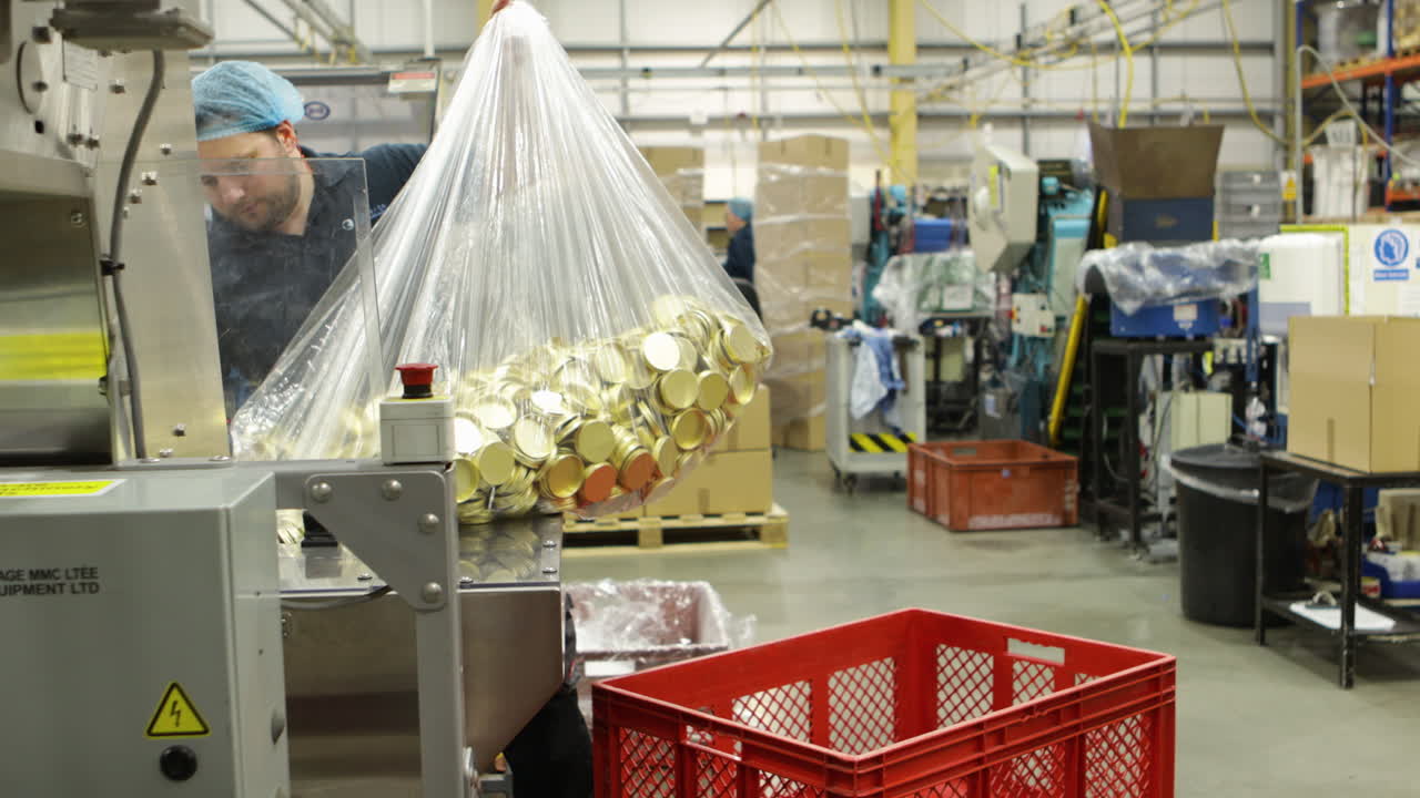 산업 공장 환경에서 큰 가방을 들고 있는 노동자, 기계가 보입니다.