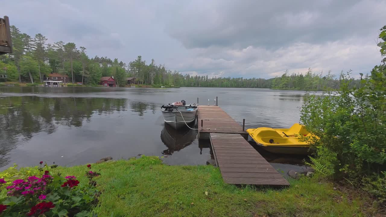 Time lapse of a pedal boat and fishing boat tied to a dock on Rainbow Lake in the Adirondacks in New York with dark clouds rapidly moving across the sky