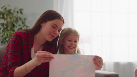 Joyful-teenage-girl-and-sister-look-at-painting-in-apartment