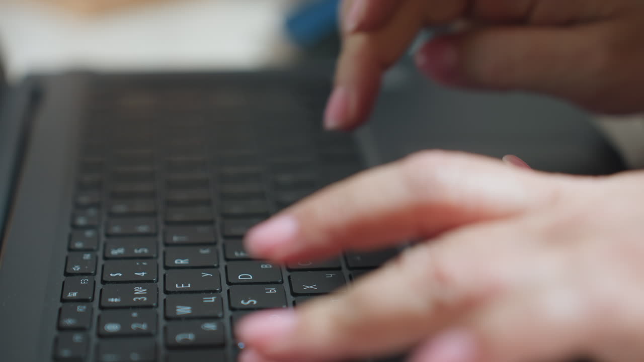 Close up of woman typing on laptop keyboard with fingers having pink painted nails, captured in soft blur background, emphasizing motion and focus during digital work environment indoors