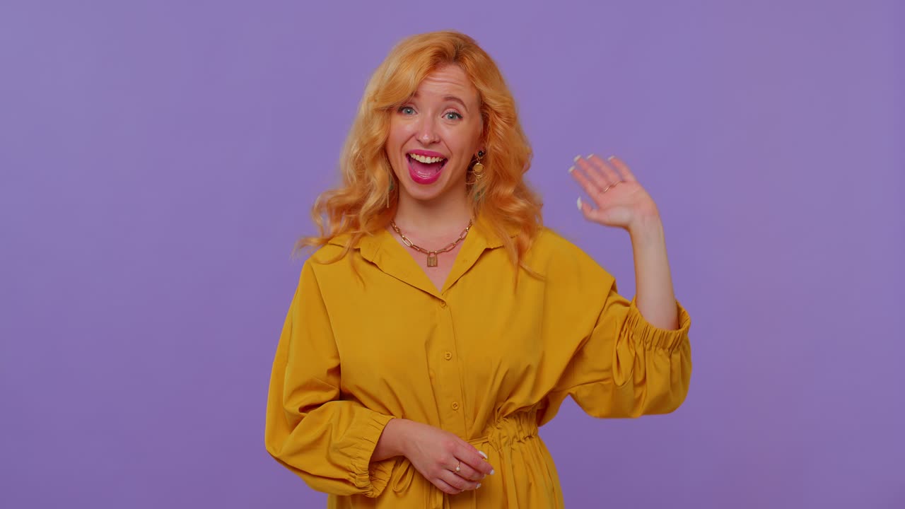chica de pelo largo sonriendo amigablemente a la cámara y agitando las manos gestando hola o adiós, bienvenida