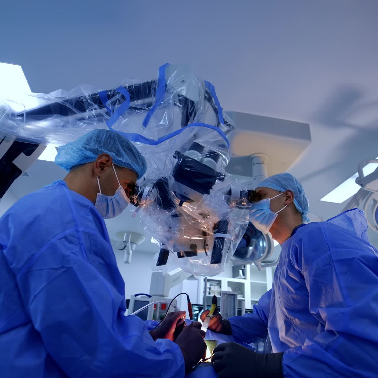 Professional neurosurgeons standing over patient using tools. Doctors perform procedure looking at microscope. Low angle view