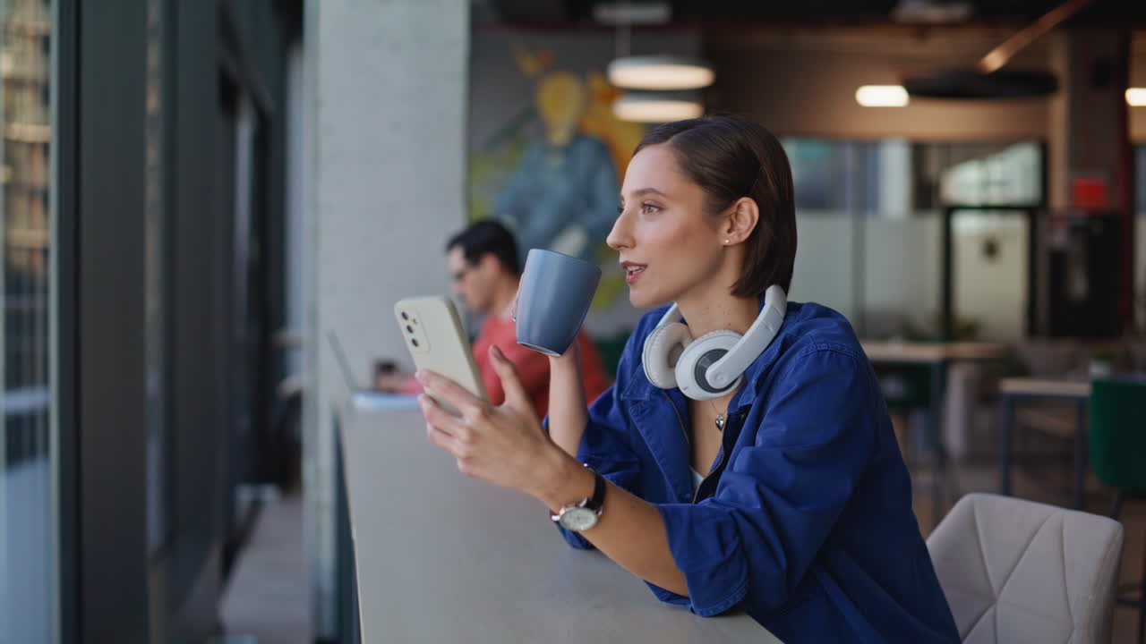 Relaxed brunette watching smartphone at coffee shop with headphones closeup
