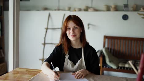 a red-haired girl draws a scheme of her product on paper with a pencil