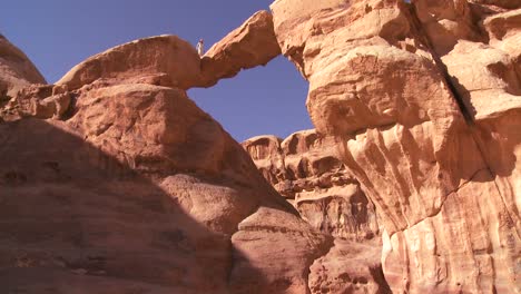 inclínate hacia una increíble formación de arco en el desierto de sadi en wadi rum jordan con un hombre beduino caminando