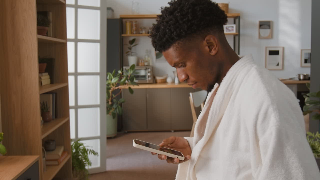 A man in a robe using his phone indoors