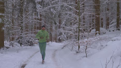 chico barbudo corriendo con traje verde neón en un bosque nevado en un camino salvaje durante el frío día de invierno - sigue la toma, hacia la cámara, cámara lenta
