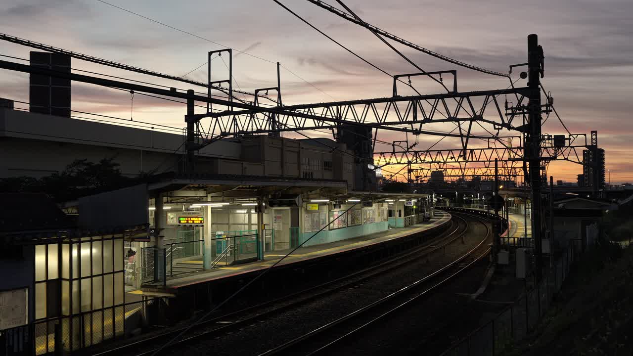 A shot of the Horikiri Station platform at dusk. Trains arrive and depart, and the urban infrastructure is illuminated