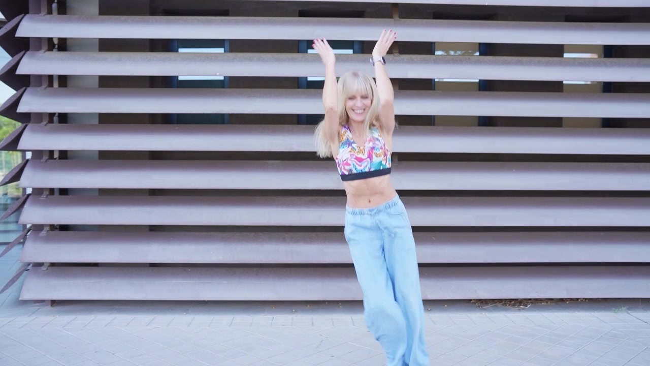 A stylish blonde woman displays dynamic dance moves in a casual outdoor setting