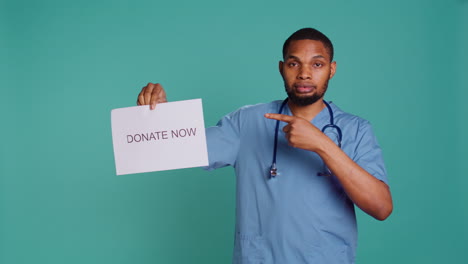 portrait of male nurse holding donate now sign, inviting people to contribute