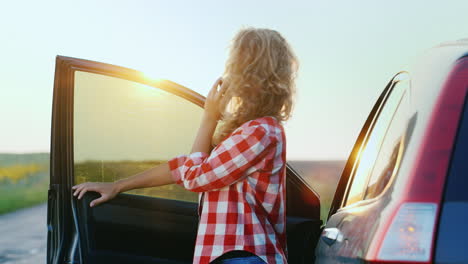 a woman is talking on the phone standing by a car