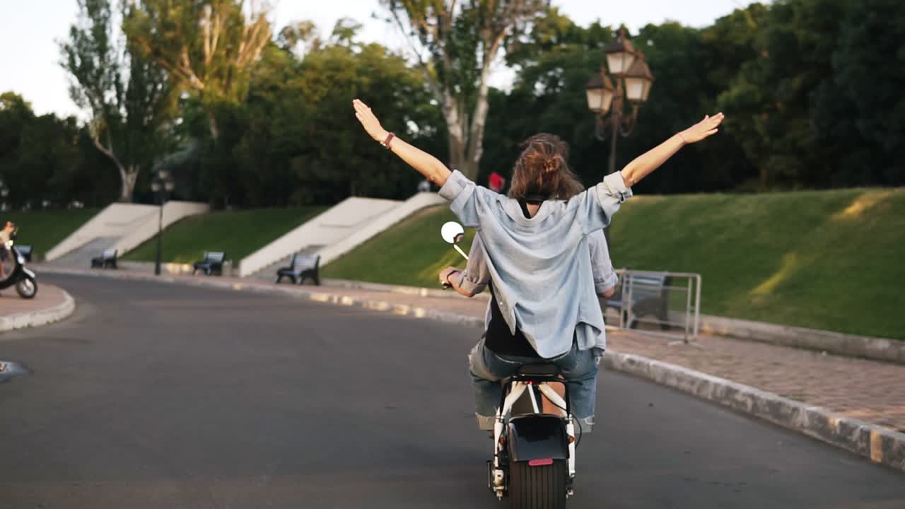 rara vista de una pareja joven montando una bicicleta eléctrica en el parque verde. niña con una camisa azul con las manos extendidas. sintiéndose libre y feliz