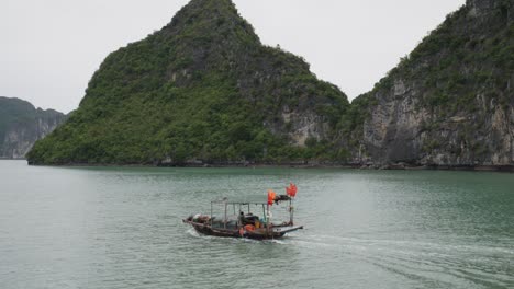 traditional boat cruising in the ha long bay passing by on limestone cliffs covered with vegetation in vietnam