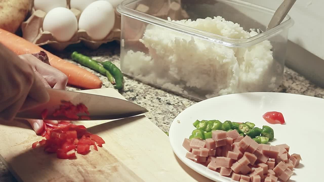 Chopping red paprika and setting it aside among diced chili and ham, preparing the ingredients for a fried rice recipe